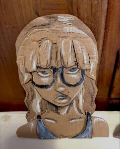 Portrait d une adolescente a lunettes, dessine a la craie blanche et noire directement sur du carton brut, puis decoupe en suivant la silhouette.